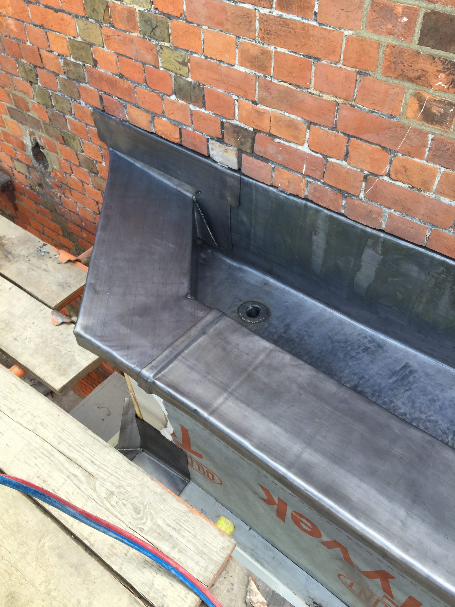 Close-up view of a finished lead-lined bay beside a brick wall, showing neatly formed leadwork with welded joints and a central outlet