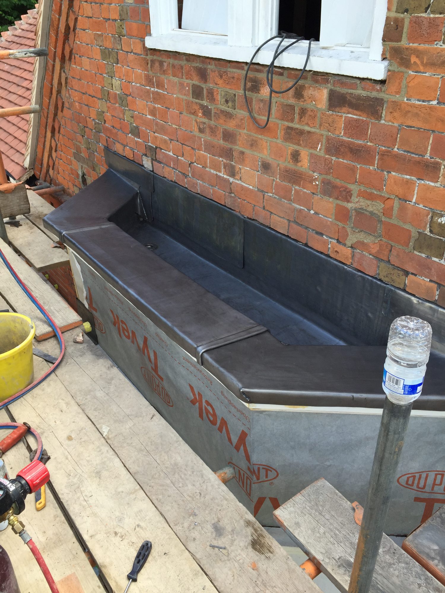 Completed lead-lined bay with neatly formed welded joints and upstands against the brick wall, viewed from the scaffold platform