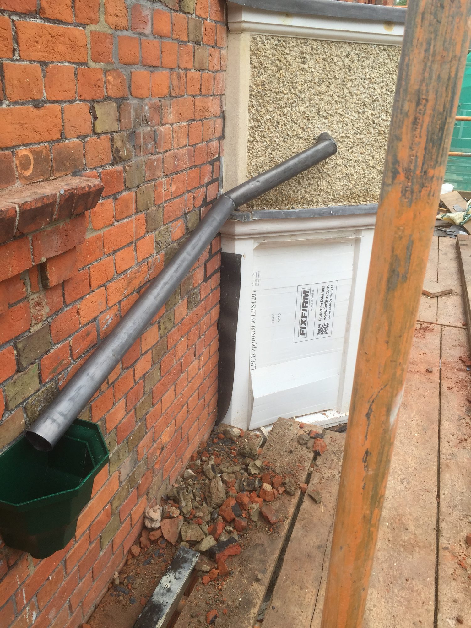 Refurbished lead pipe with a formed joint running from the brick wall towards the adjacent building, viewed from scaffold level