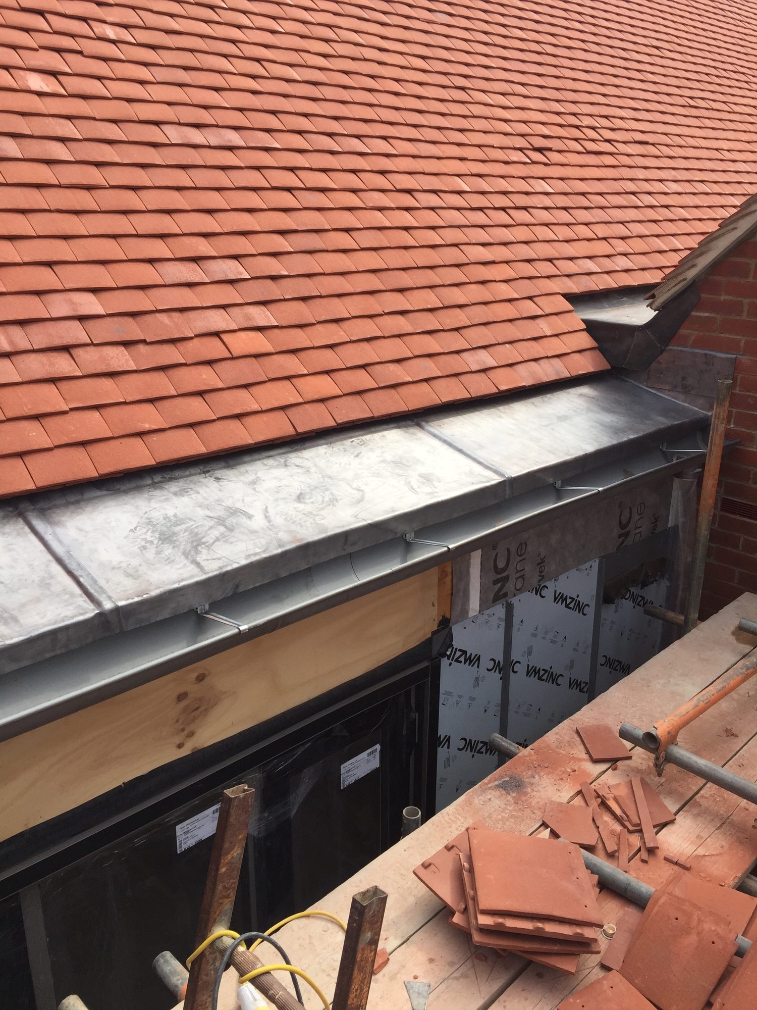 Completed lead-lined roof valley beneath a tiled roof, with formed joints and surrounding roof tiles visible from the scaffold platform