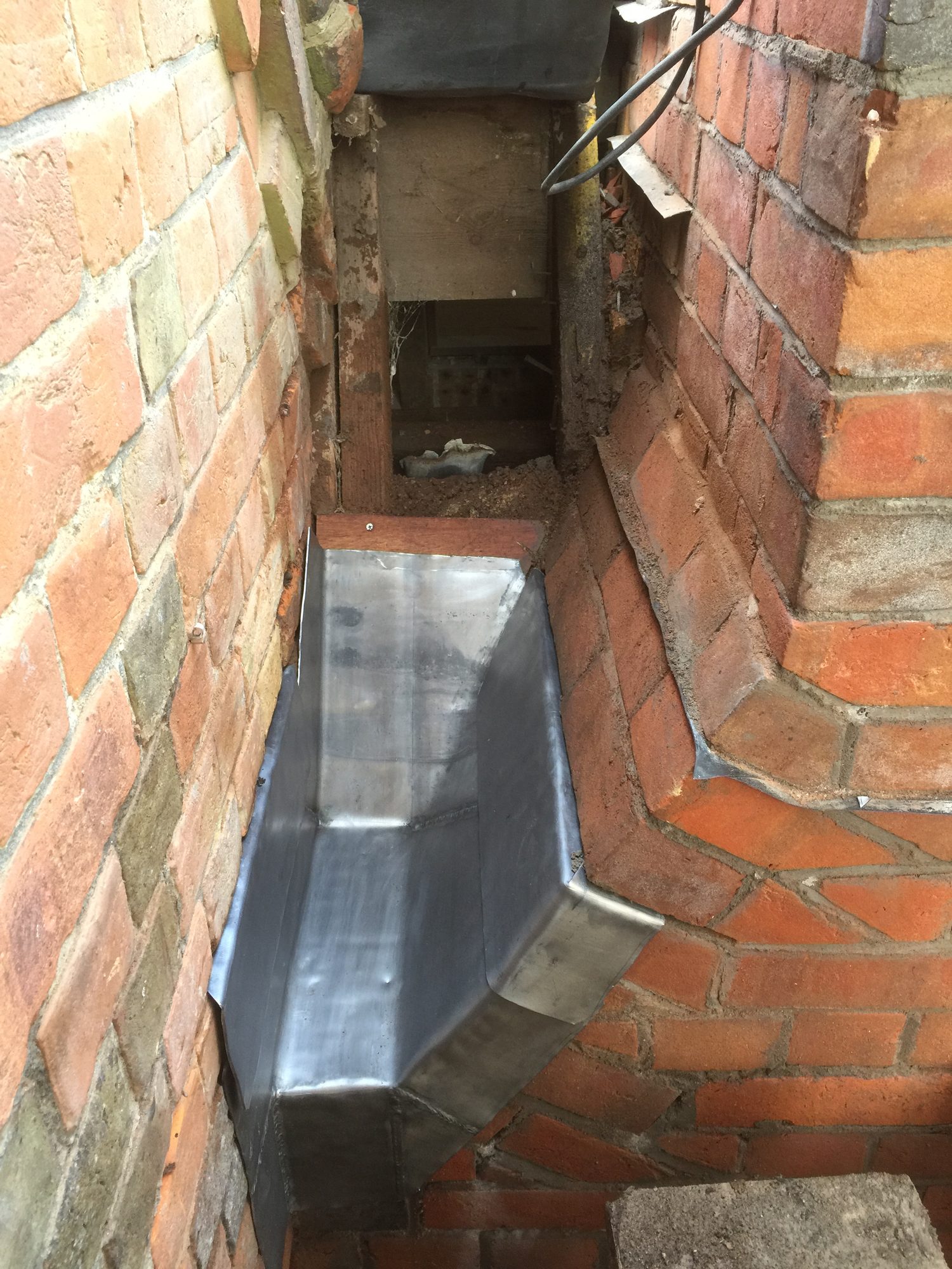 Close-up of completed dark grey welded leadwork fitted between two brick walls, with raised sides, formed corners and visible welded joints