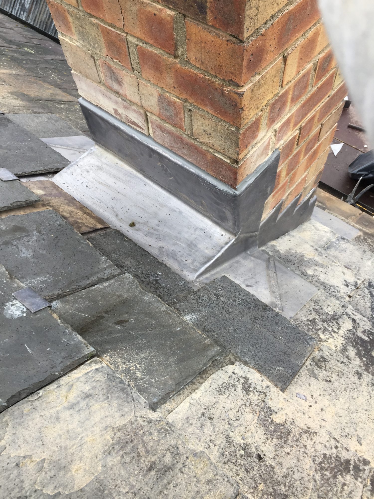 Close-up view of a brick chimney with newly finished lead weathering around its base, neatly dressed against the surrounding slate roof