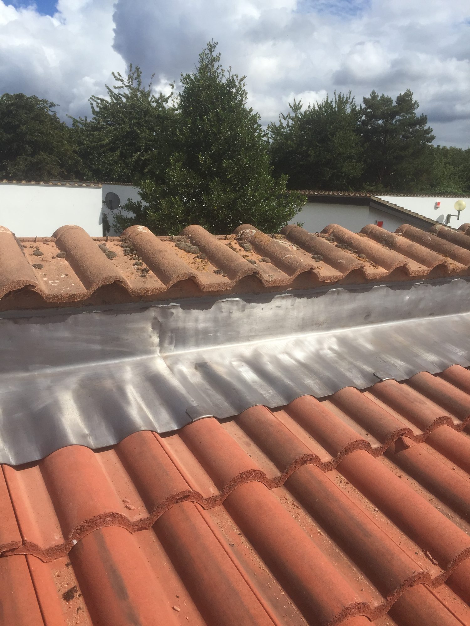 Close view of neatly formed leadwork extending across the roof junction, with overlapping tile courses and the adjoining roof tiles visible above and below