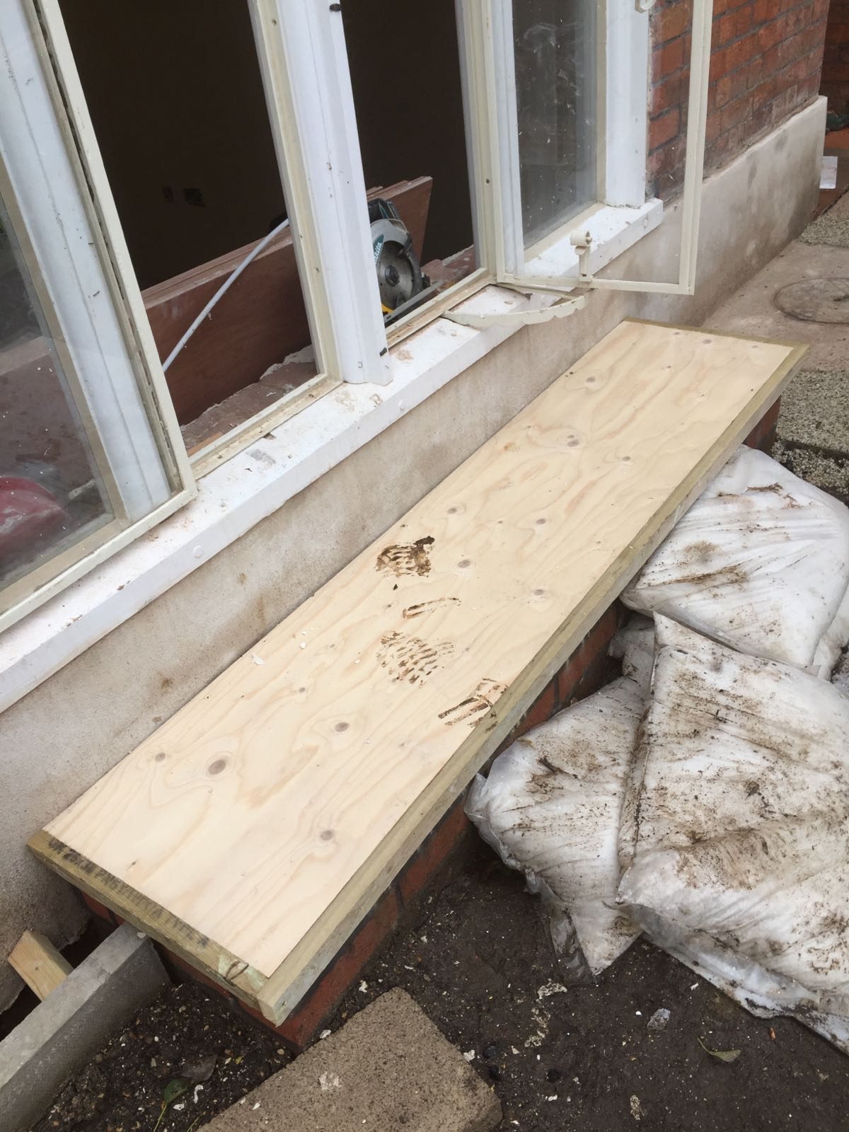 Timber boarding fitted over a brick bay beneath white-framed windows, with construction materials and protective sheeting visible around the work area