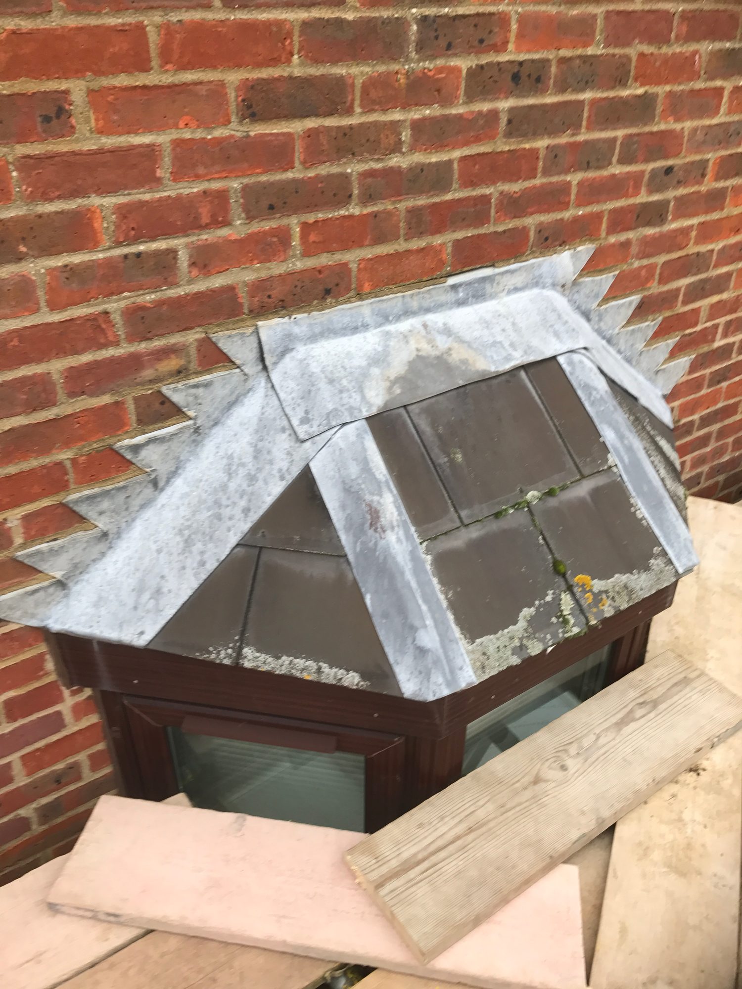 Close-up view of existing leadwork around the pitched bay window roof, with lead strips and flashing visible over the roof tiles and brickwork
