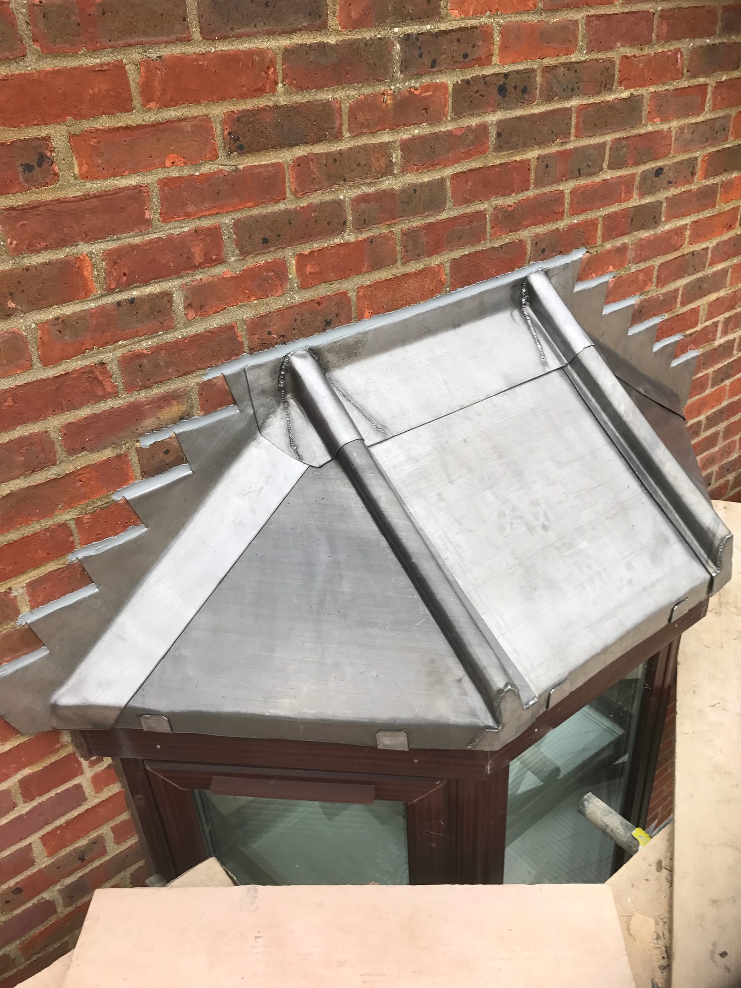 Overhead view of the completed lead roof showing formed rolls, stepped flashing and neatly finished lead detailing around the bay window