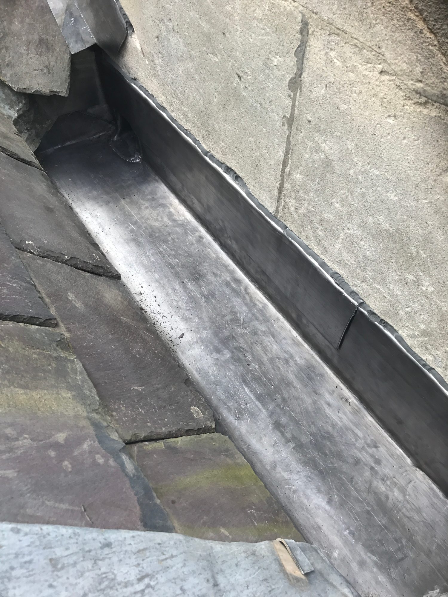 Close-up of a completed lead-lined gutter between slate roof surfaces, showing formed sides and neatly finished joints