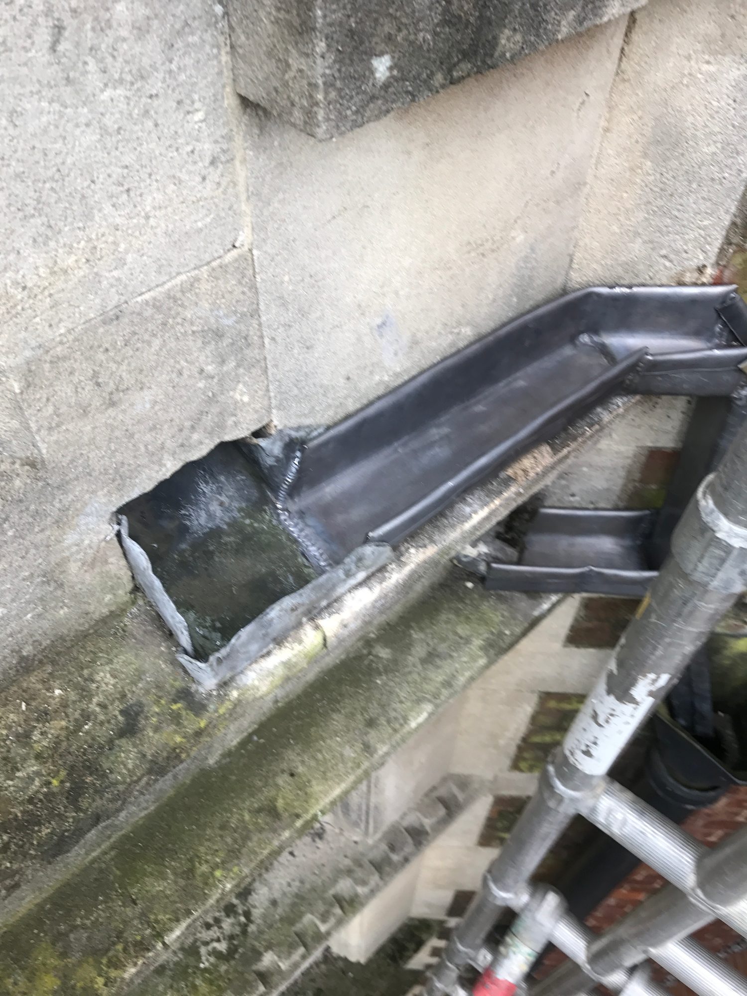 Close-up of repaired lead guttering at the edge of the roof, showing formed sections, seams and surrounding slatework