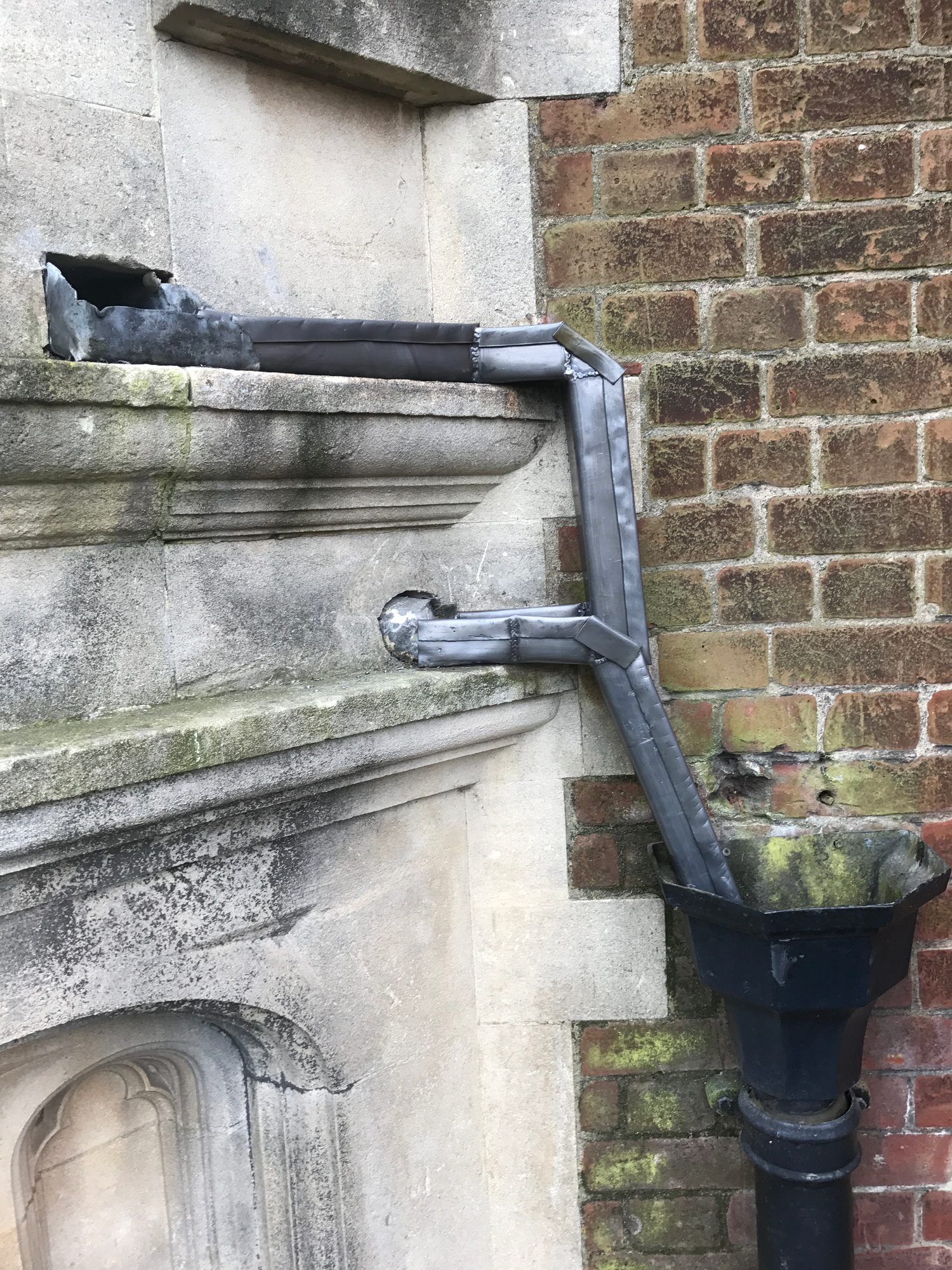 Completed lead gutter running along the stonework and connecting to a vertical lead downpipe beside the brick wall