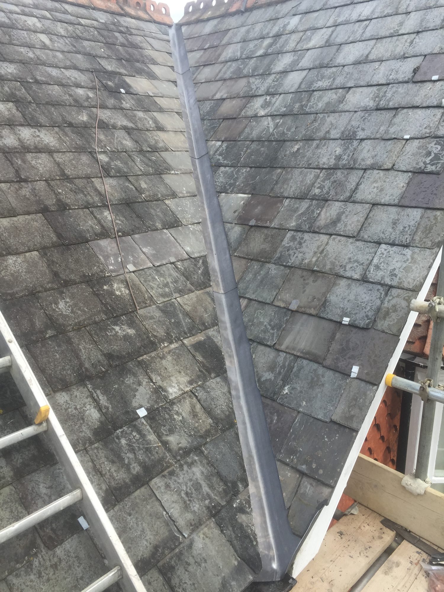 Wide view of a completed lead-lined valley running between two slate roof slopes, with the leadwork neatly fitted along the junction