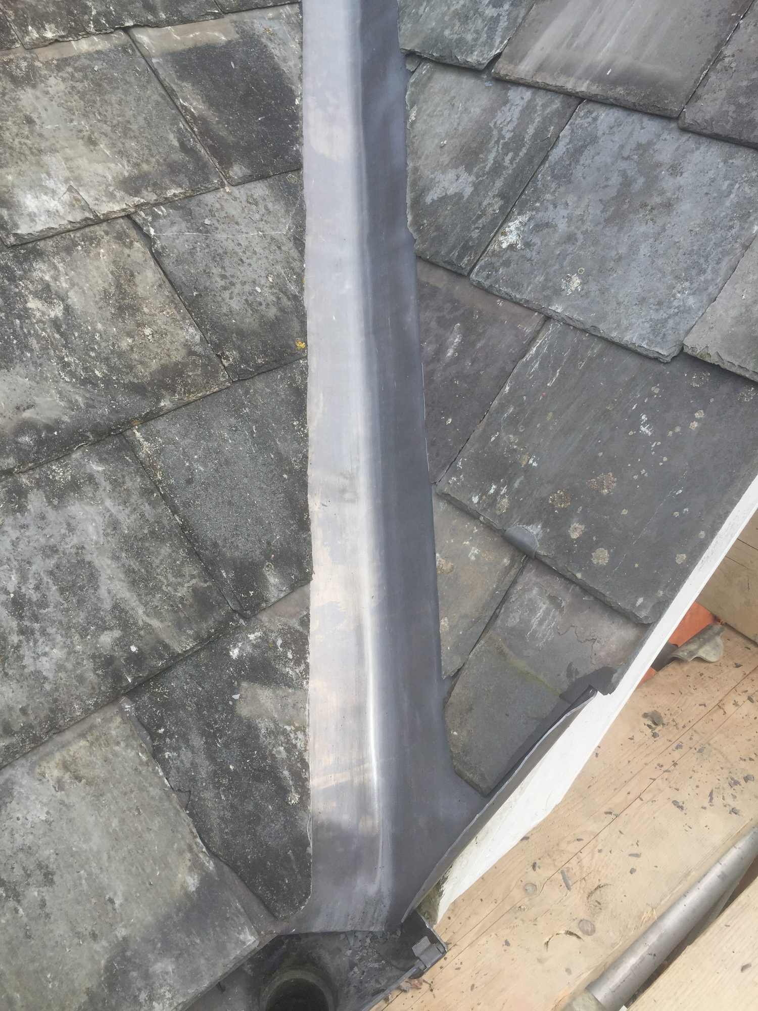 Close-up view of the completed lead valley showing the formed leadwork between the slate roof slopes and the roof edge