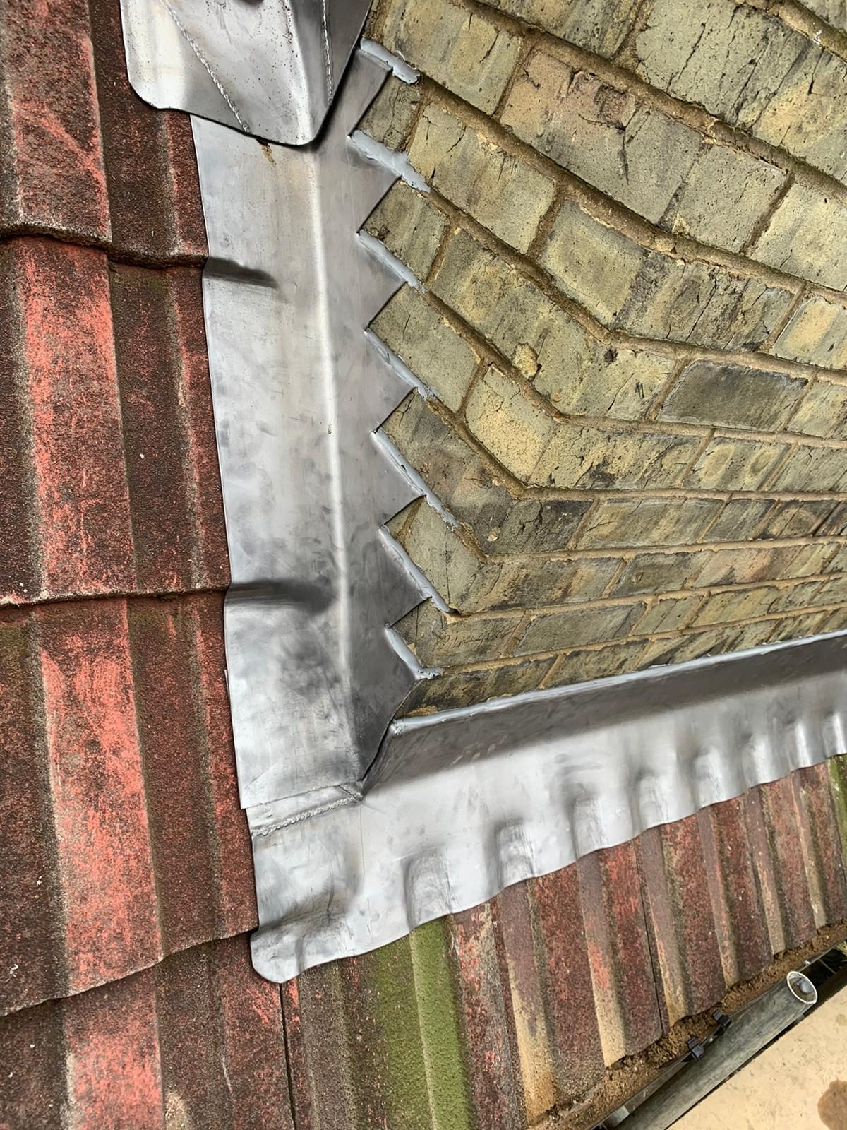 Detailed view of lead flashing running alongside a brick wall and across the adjoining roof, showing neatly formed edges, joints and stepped sections