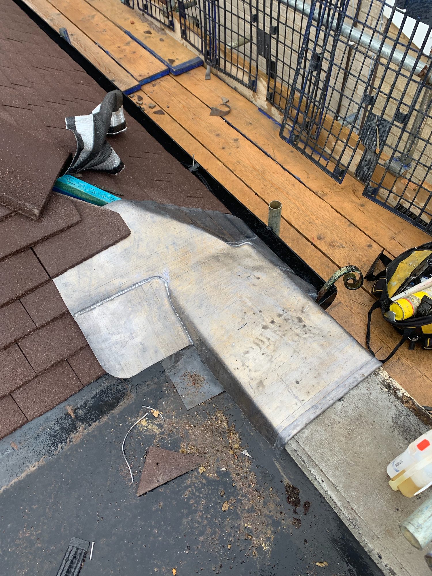 Close view of shaped leadwork extending across the junction between the roof coverings, with formed seams and overlapping sections visible alongside the scaffold walkway