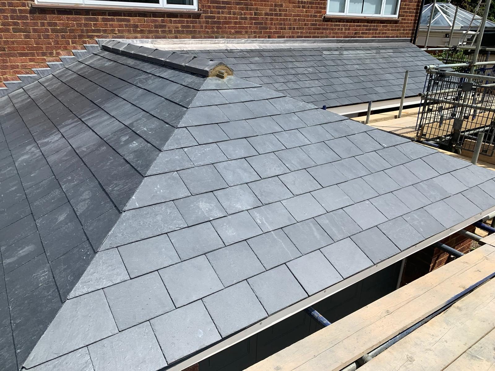 Close view of the completed low-pitch roof showing neat rows of slate tiles, a sharply defined mitred hip and lead detailing along the upper roof junction