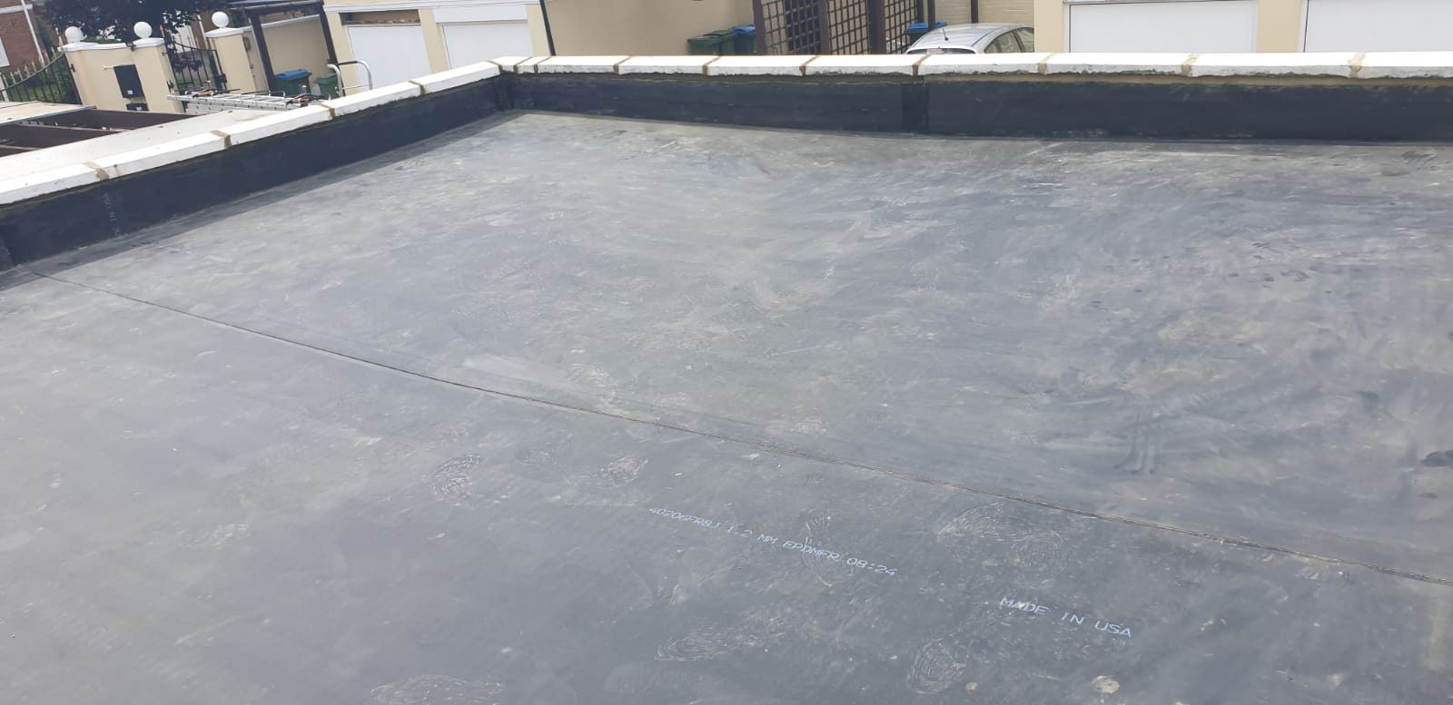 Wide view of the completed flat roof showing a smooth dark grey roof surface with visible seams and dark perimeter detailing