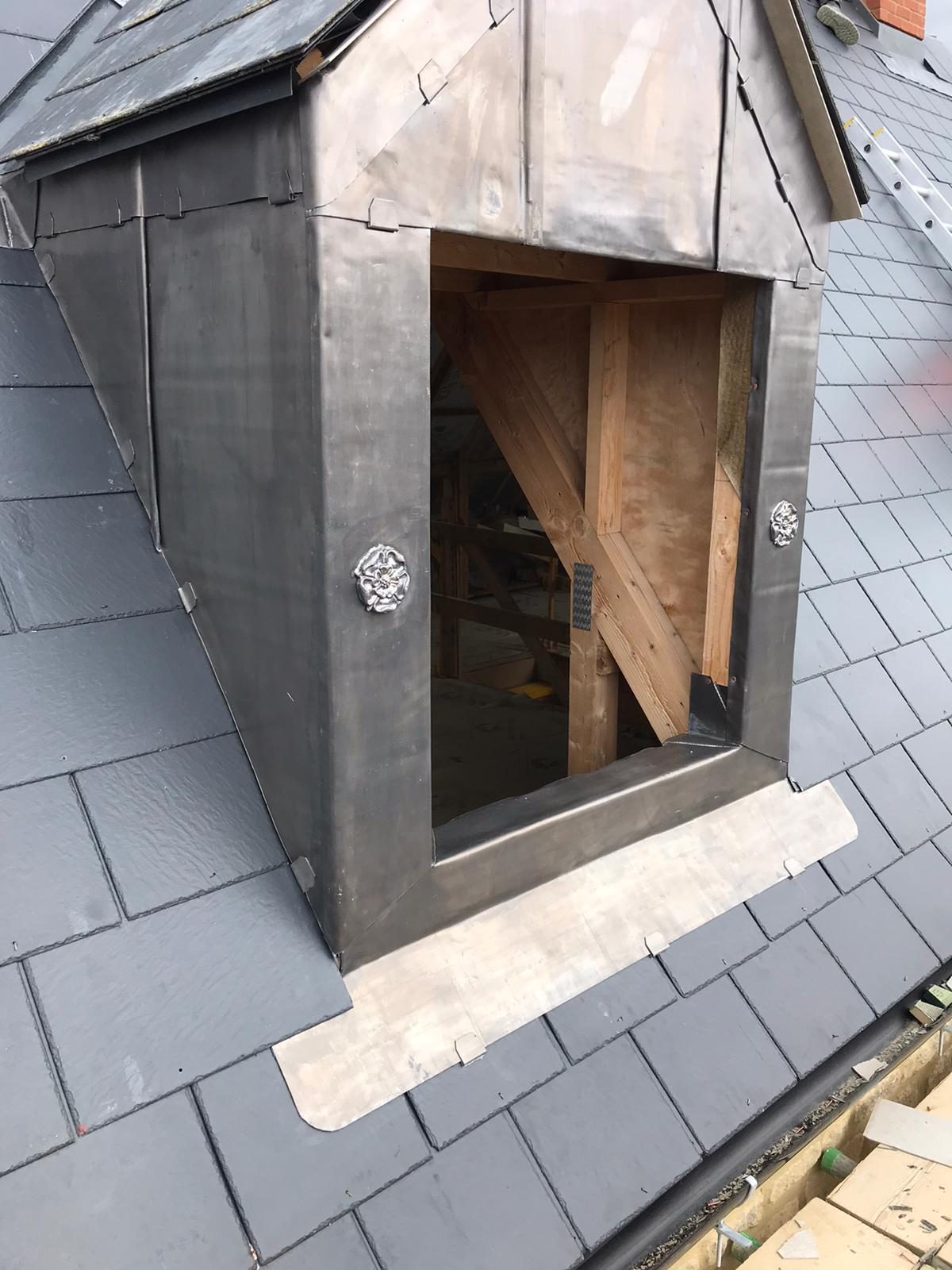 Front view of the dormer showing lead-clad sides and roof face, slate roofing around the structure and timber framing visible through the opening