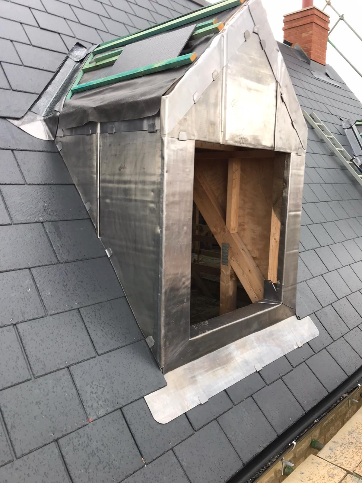 Oblique view of the dormer showing lead cladding around the front and side, slate roof tiles surrounding the structure and temporary roof access equipment above