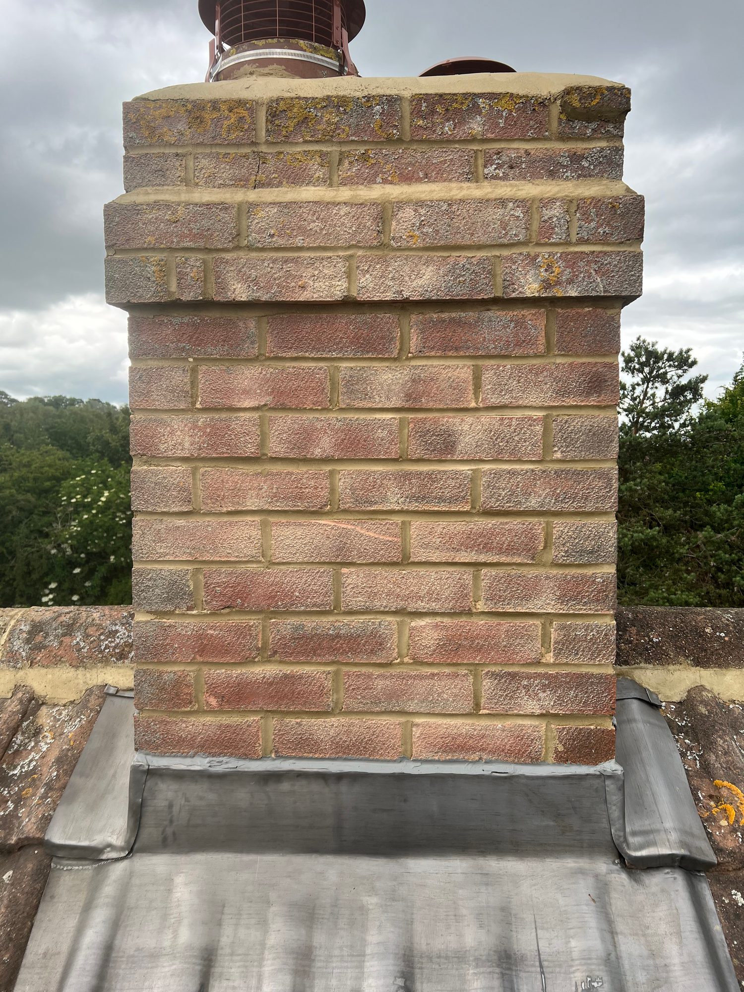 Completed - Completed chimney with repointed brickwork and new lead flashing around the base, with the tiled roof visible