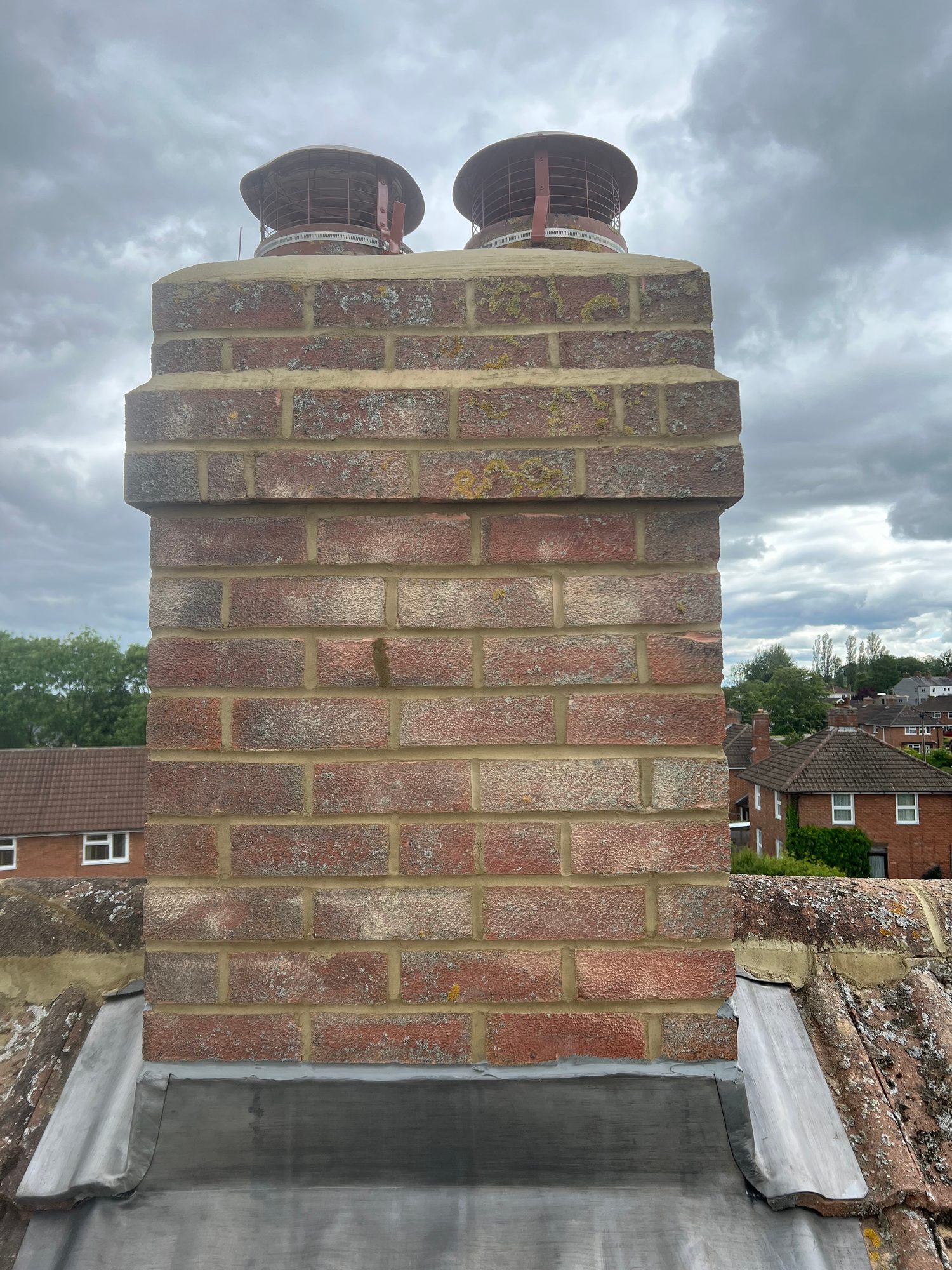 Completed - The completed brick chimney stack showing renewed mortar joints, lead flashing and protective cowls fitted to the chimney pots