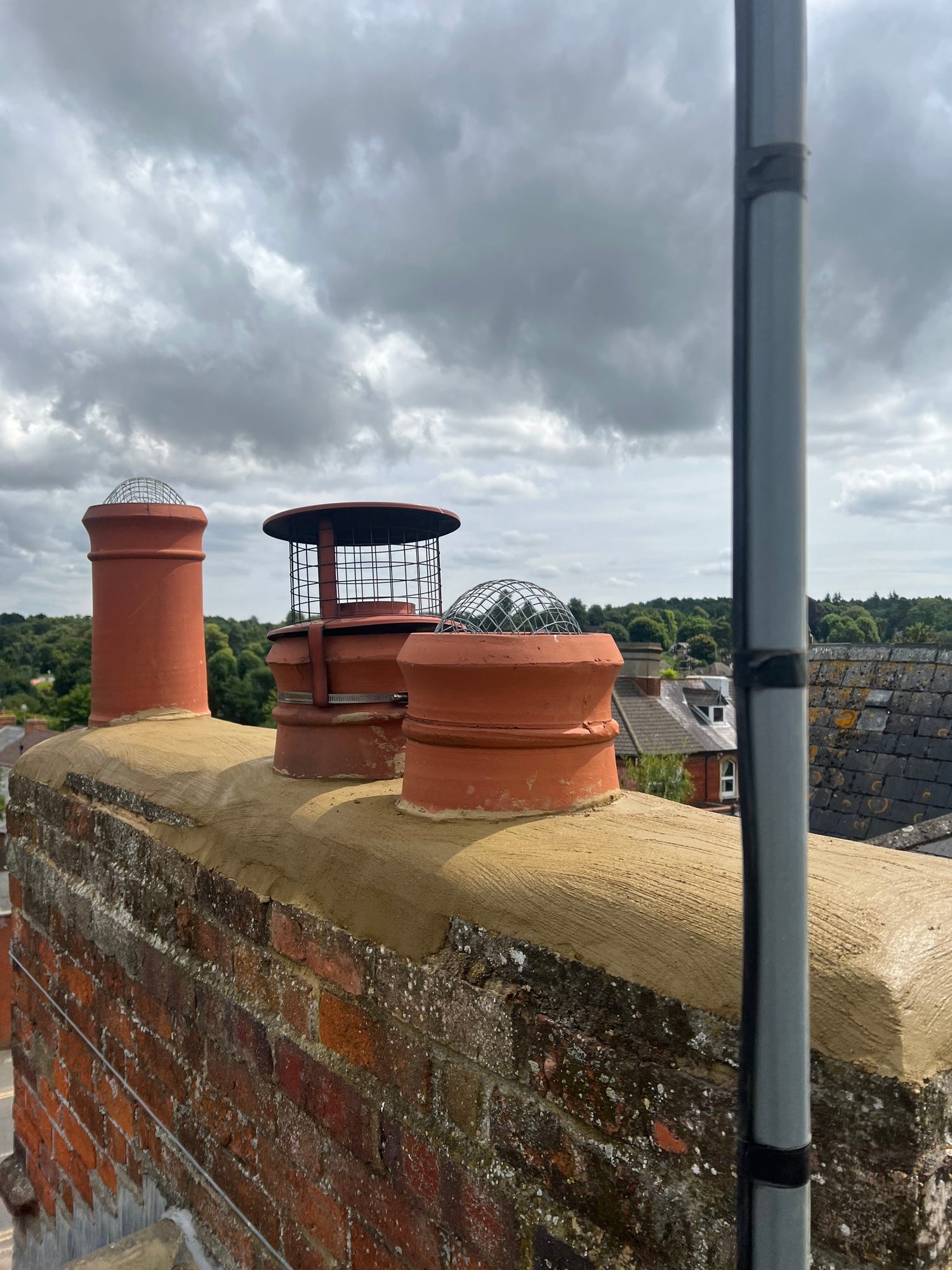 Completed - Completed roof showing multiple terracotta chimney pots with protective bird guards and renewed mortar detailing to the brick chimney stack
