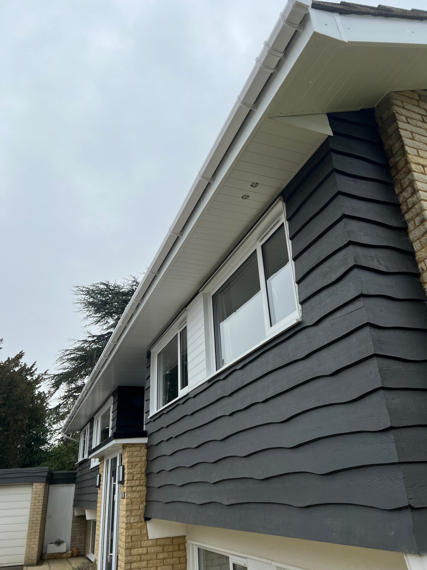 Completed - The completed dark cladding and white-framed windows with new white soffits, fascia and guttering along the side of the property