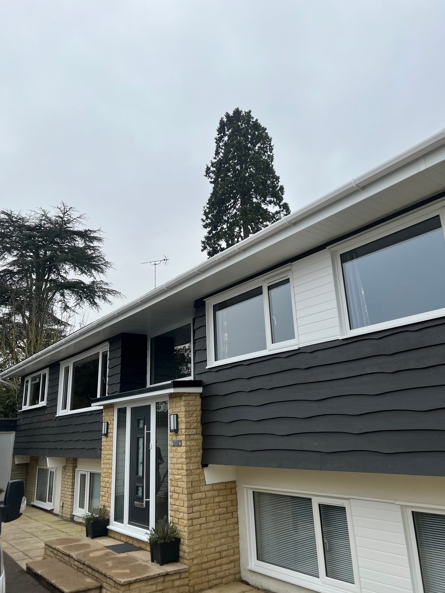 Completed - The completed front of the property showing the dark cladding, white-framed windows and doors, brickwork, soffits, fascia and guttering