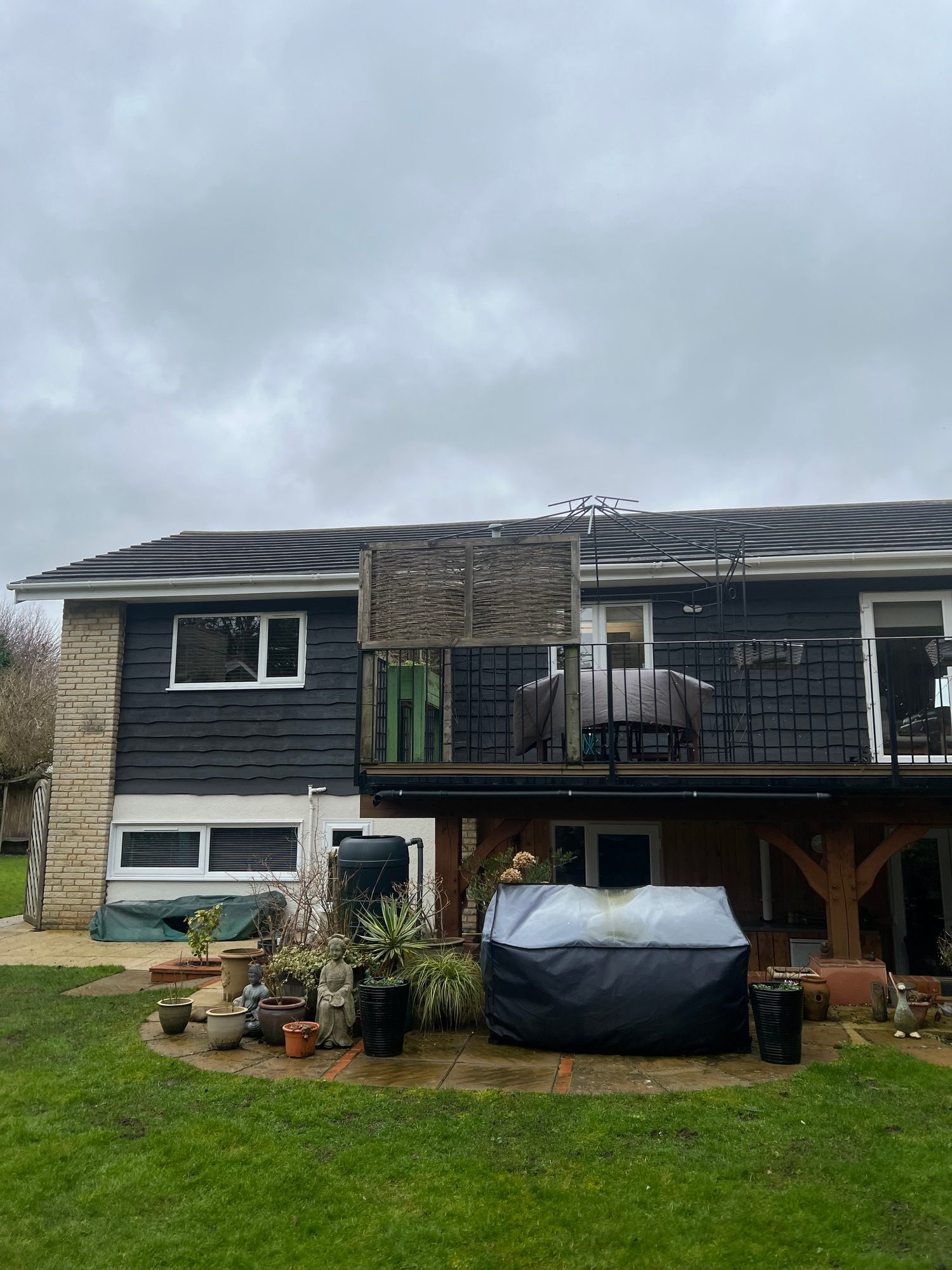Completed - The completed rear of the property showing the dark exterior cladding, brickwork, white-framed windows, balcony and timber supports