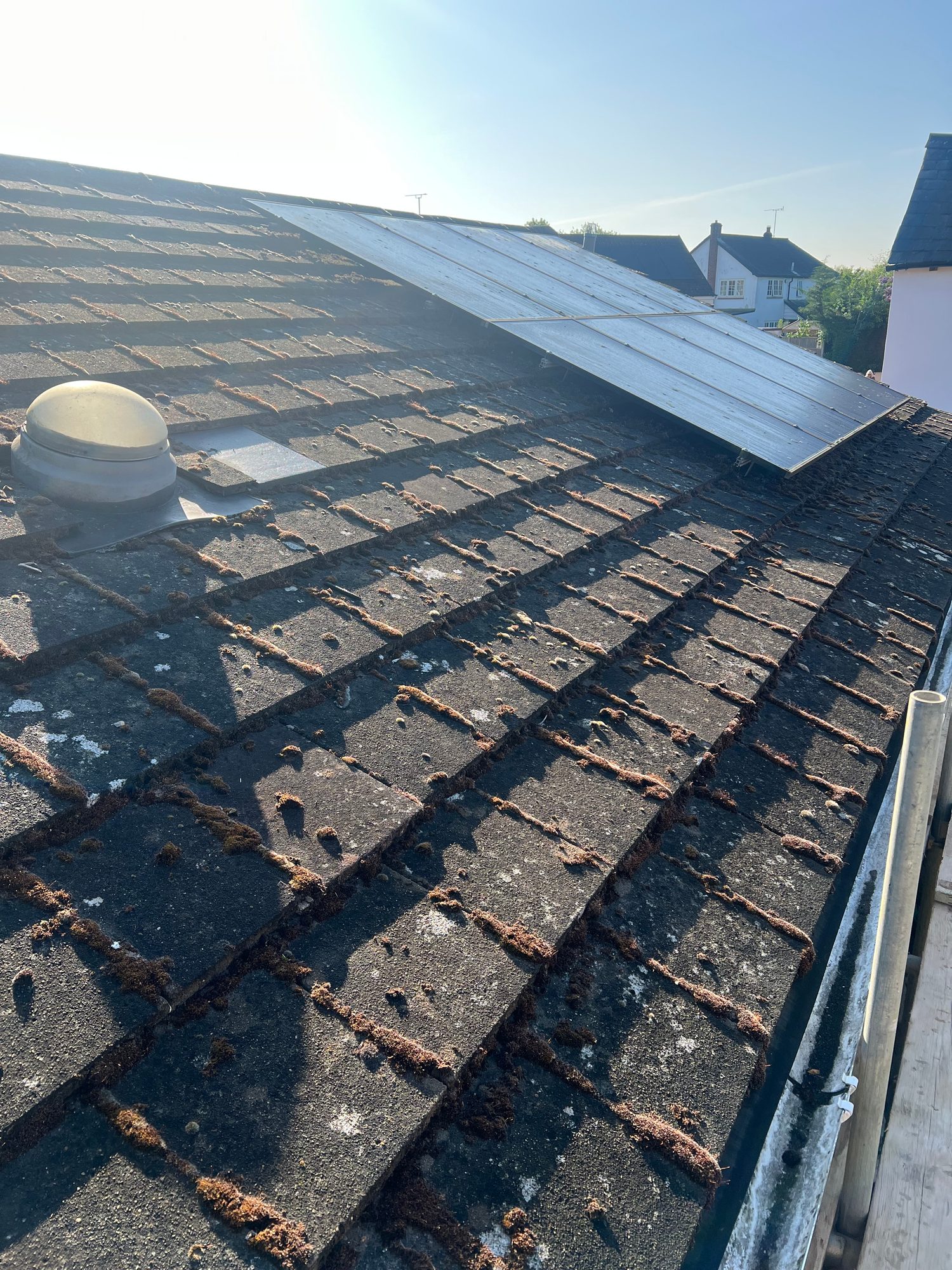 Sloping tiled roof with weathered roof tiles, a roof vent and a row of solar panels visible across the upper section