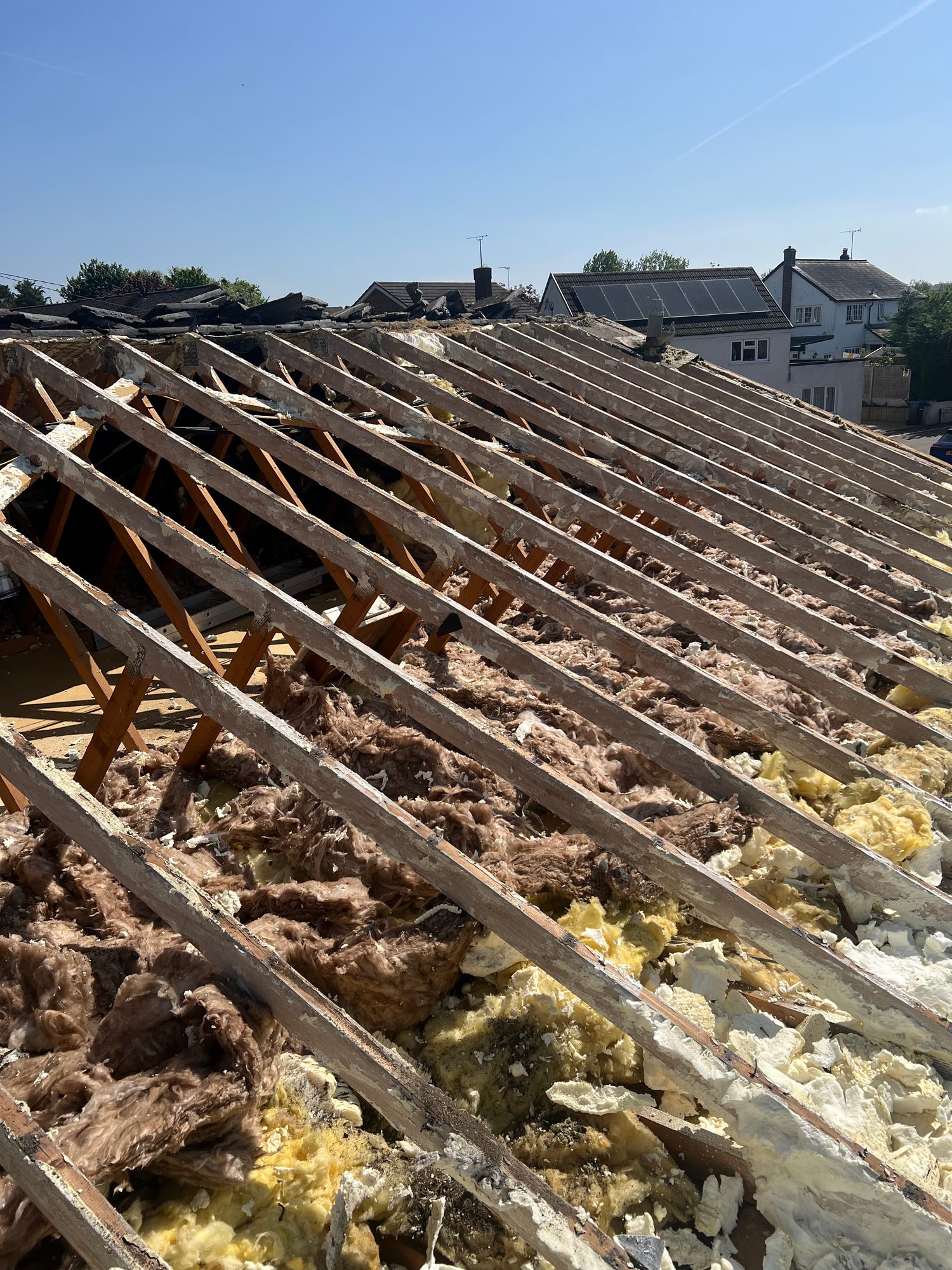 Wide view of the roof with the covering removed, showing timber rafters and sections of existing fibreglass and foam insulation