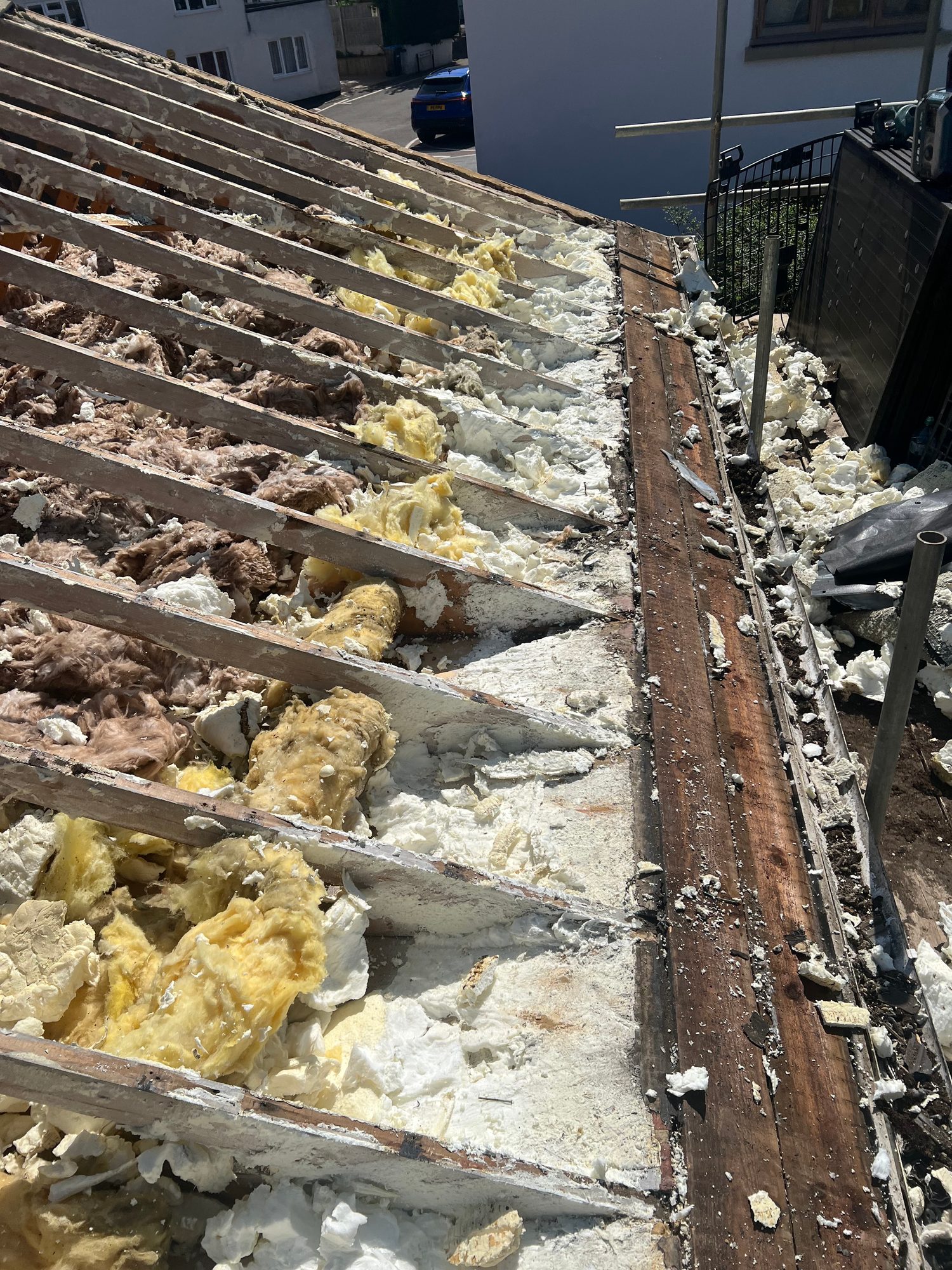 Sloping roof section showing exposed timber rafters, mixed insulation materials and a timber edge section alongside the scaffolding