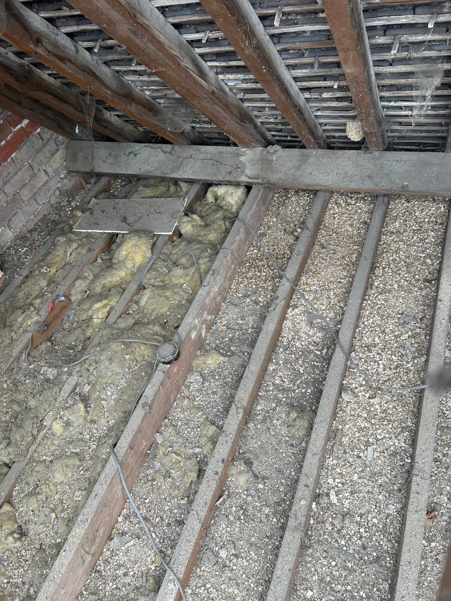 View beneath the roof showing timber rafters, old insulation, loose material and electrical cabling between the roof timbers