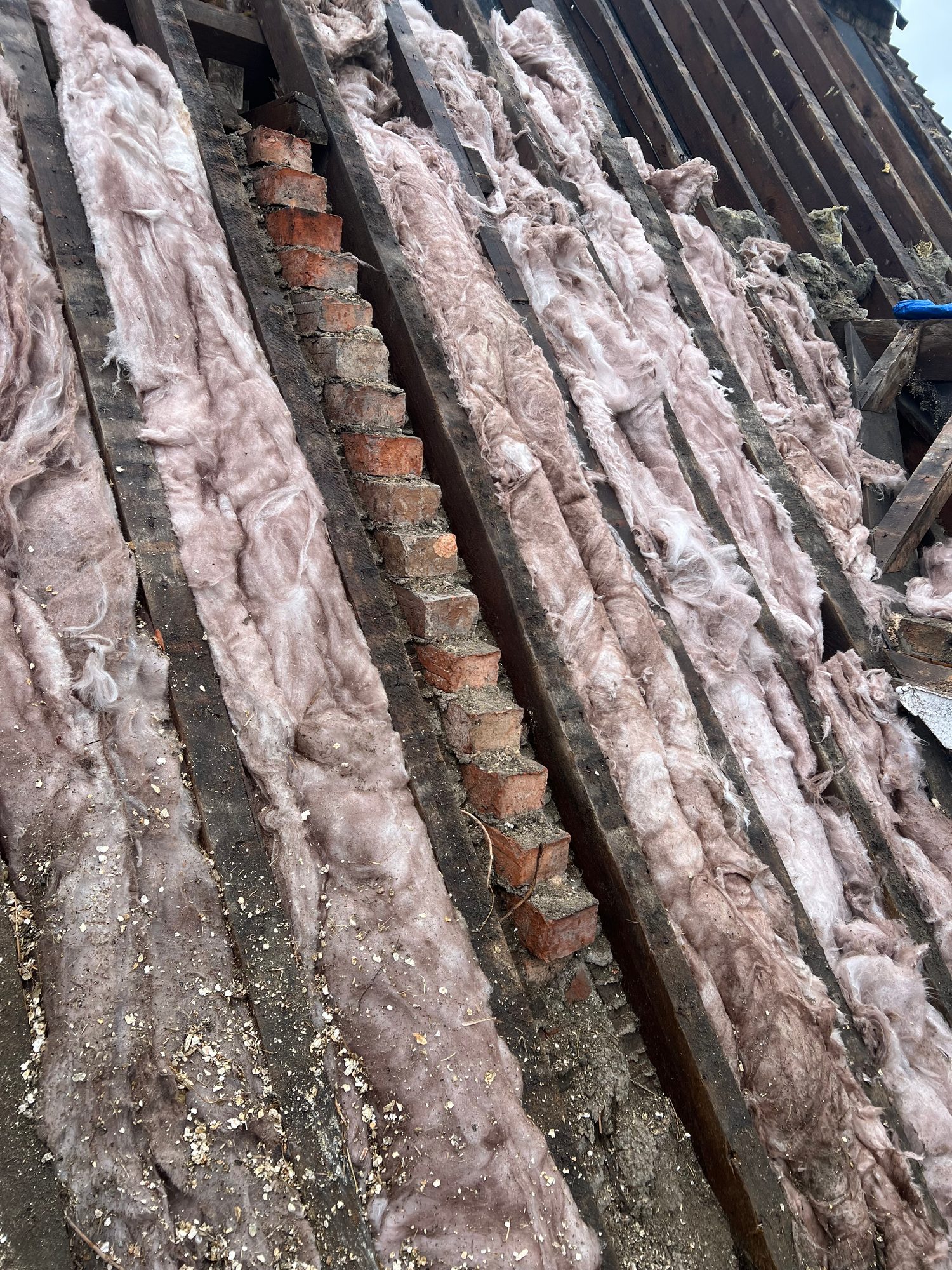 Close view of old fibreglass insulation between timber roof members, with exposed brickwork and roof battens visible