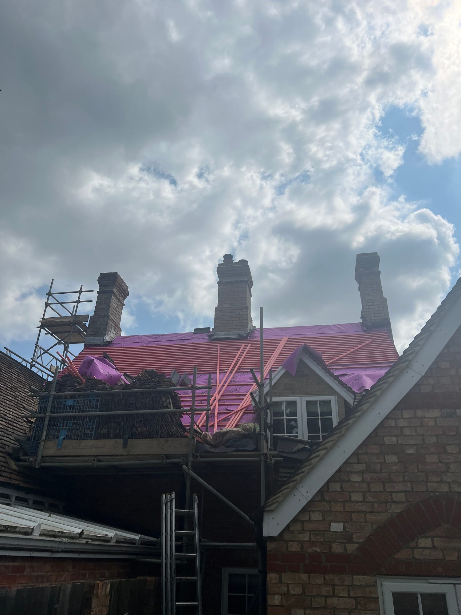 View of the building showing a section of roof covered with new red roofing material, with scaffolding and existing chimneys visible