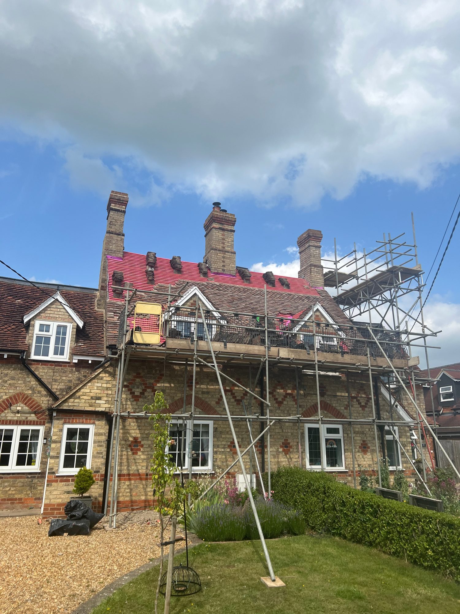Wide view of the building with scaffolding surrounding the roof, new red roofing material visible across the upper roof and existing tiled sections remaining below