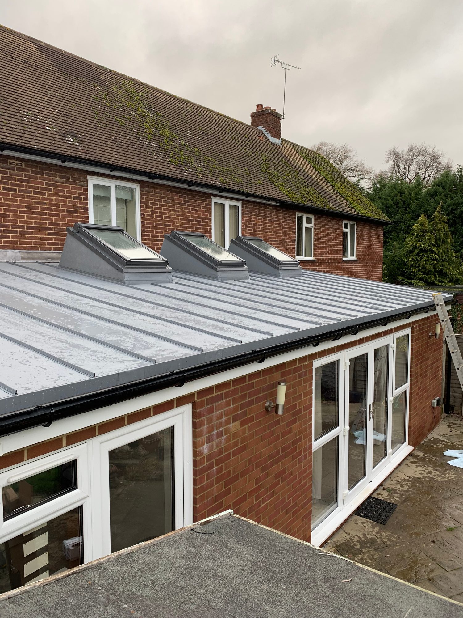Completed roof extension with grey standing seam metal roofing, three rooflights and black guttering