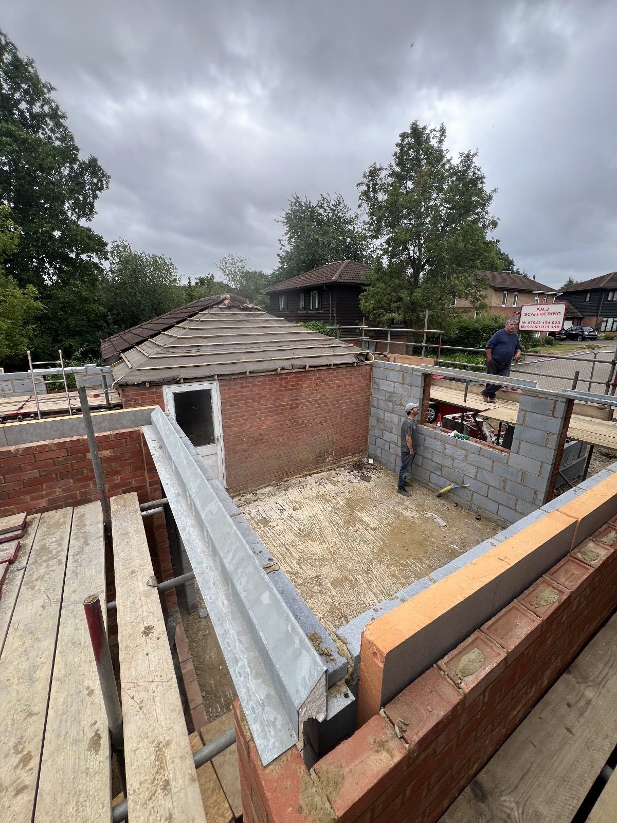 Elevated view of the existing garage roof, brick and blockwork walls, scaffold platforms and workers within the construction area