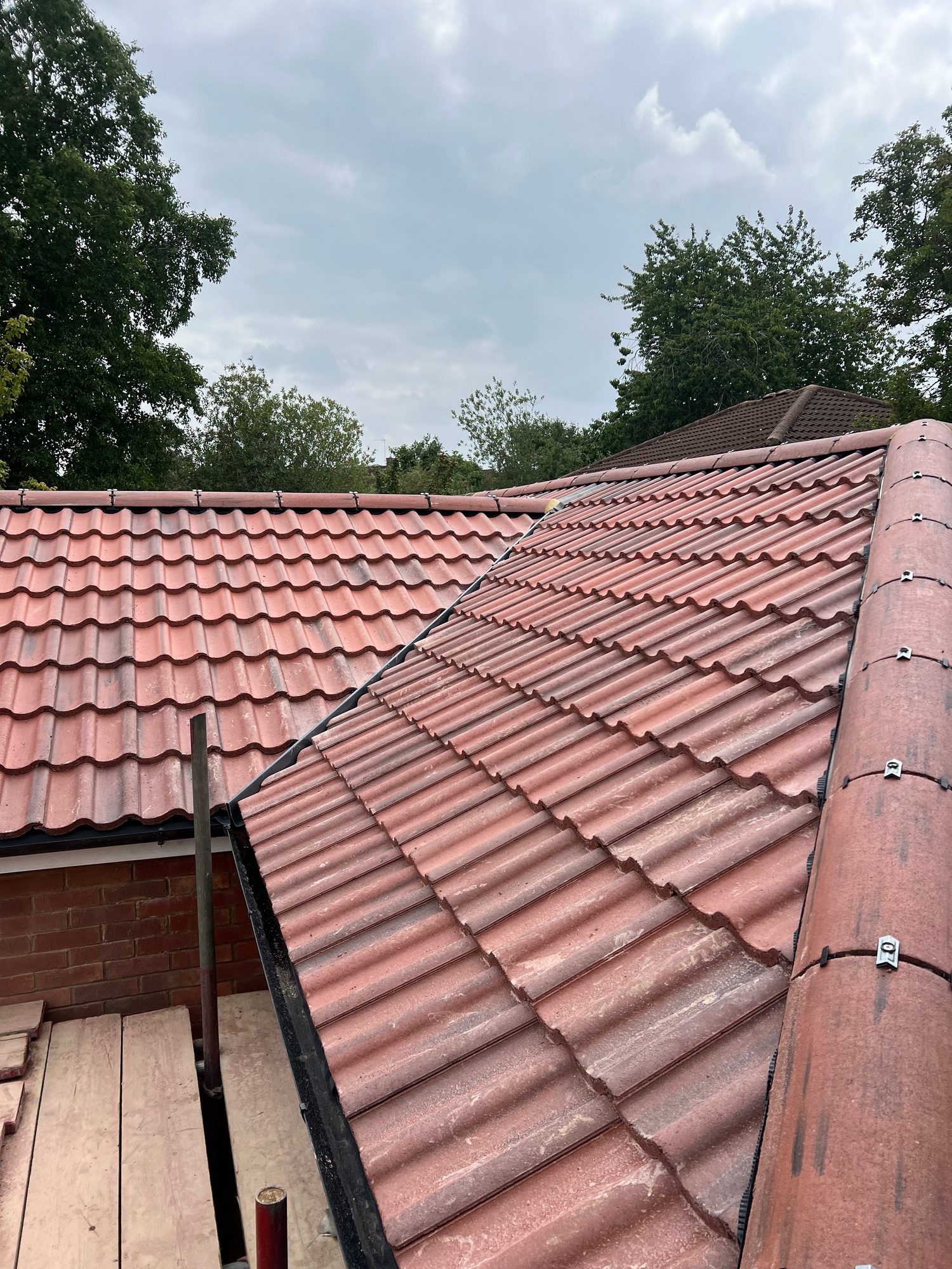 Close view of the completed red tiled roof showing rows of interlocking tiles, secured ridge tiles and black detailing along the roof junctions