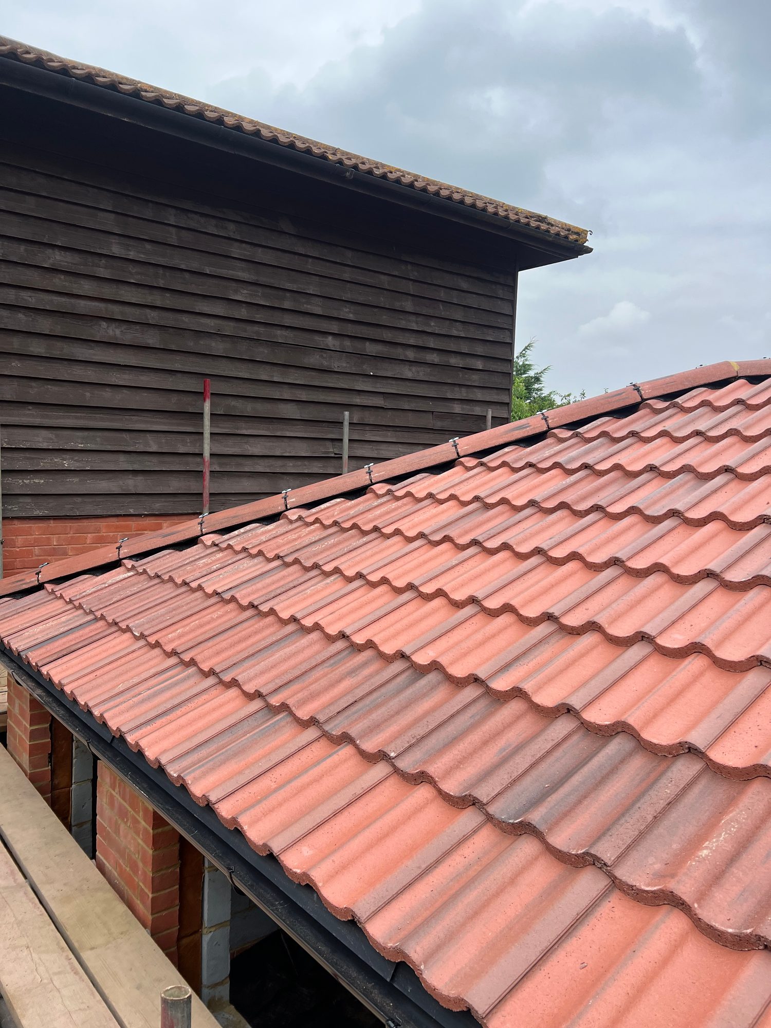 View across the completed red tiled roof showing evenly laid interlocking tiles, secured ridge tiles and black roofline detailing