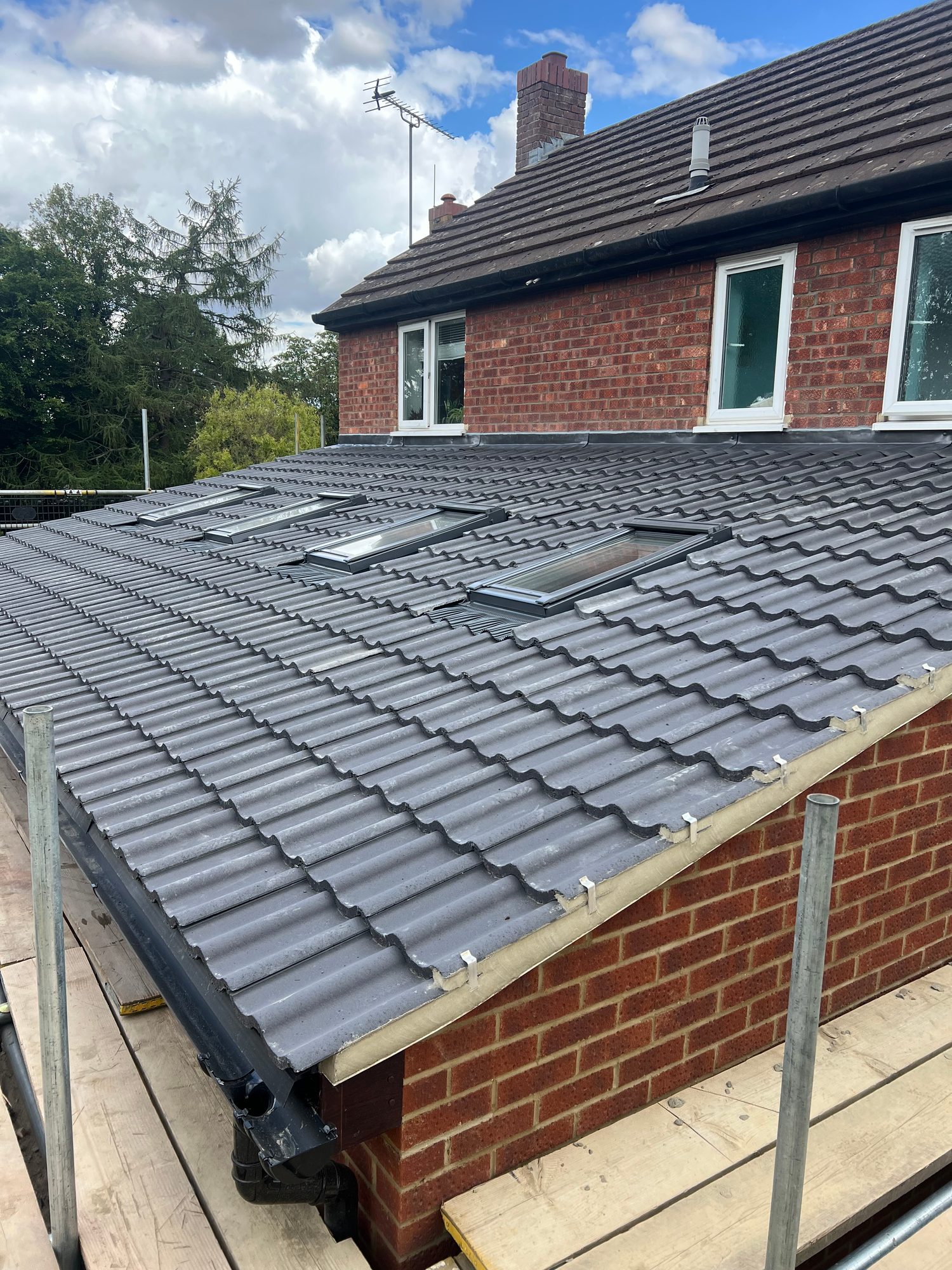 Completed extension roof with grey tiled covering, multiple rooflights, guttering and roof junction with the existing brick building