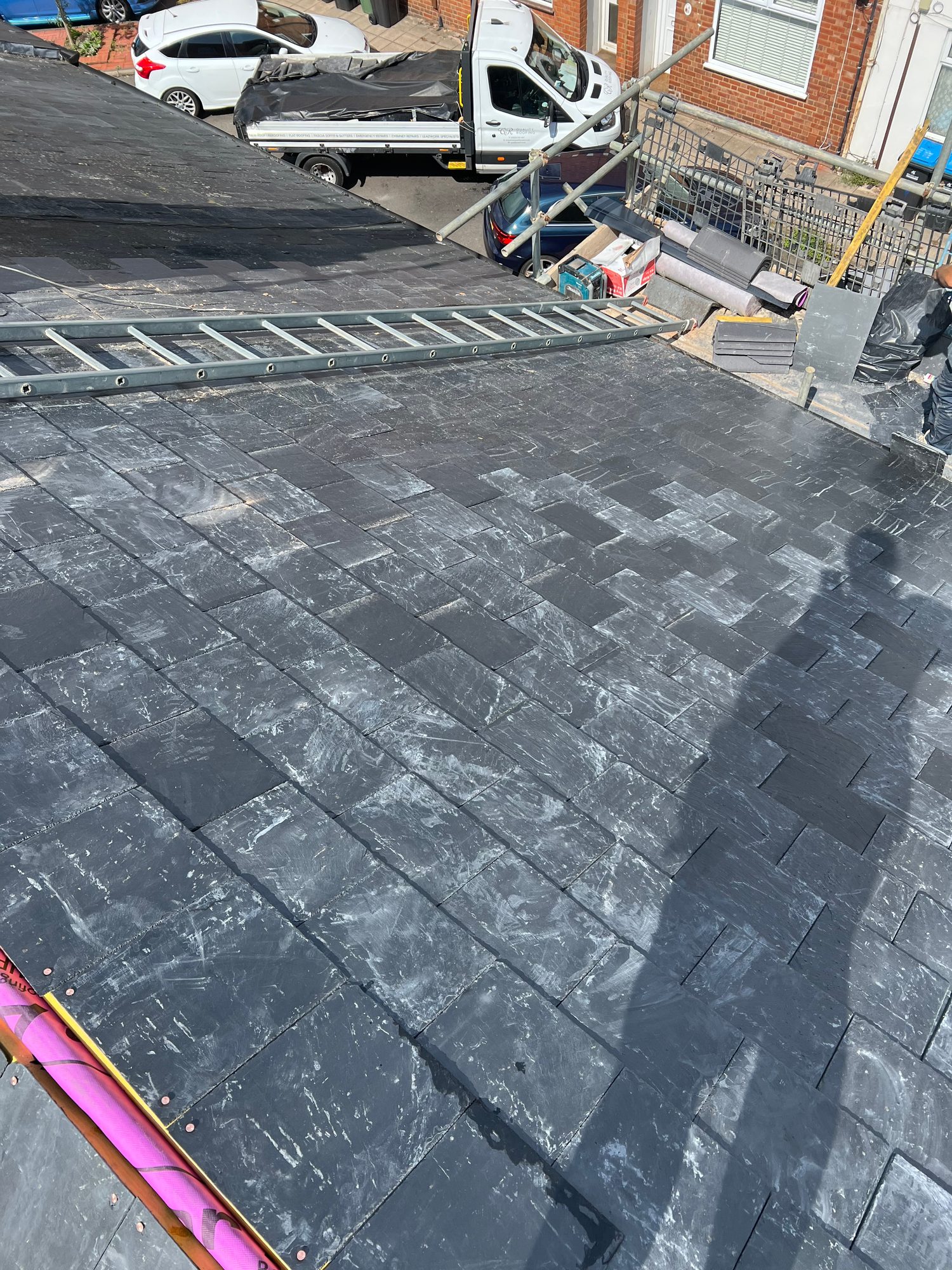 Dark slate-tiled roof with a roof ladder laid across the tiles and scaffolding along the roof edge