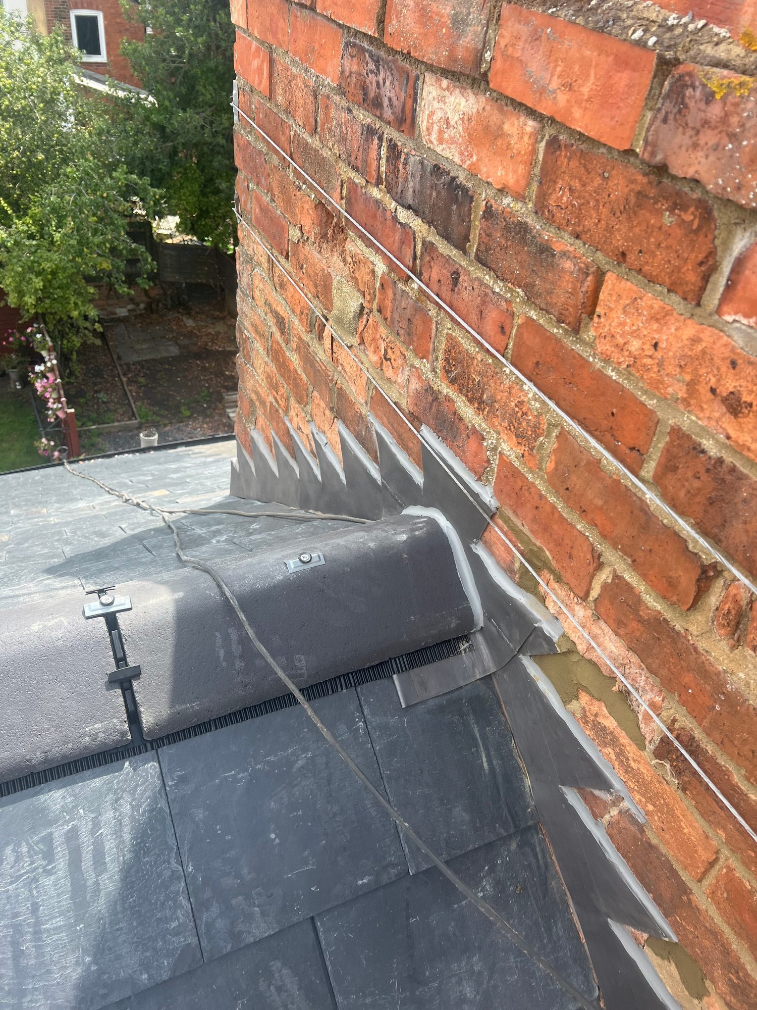 Close-up view of the completed slate roof meeting a brick chimney, showing the slate tiles and finished detailing around the chimney base