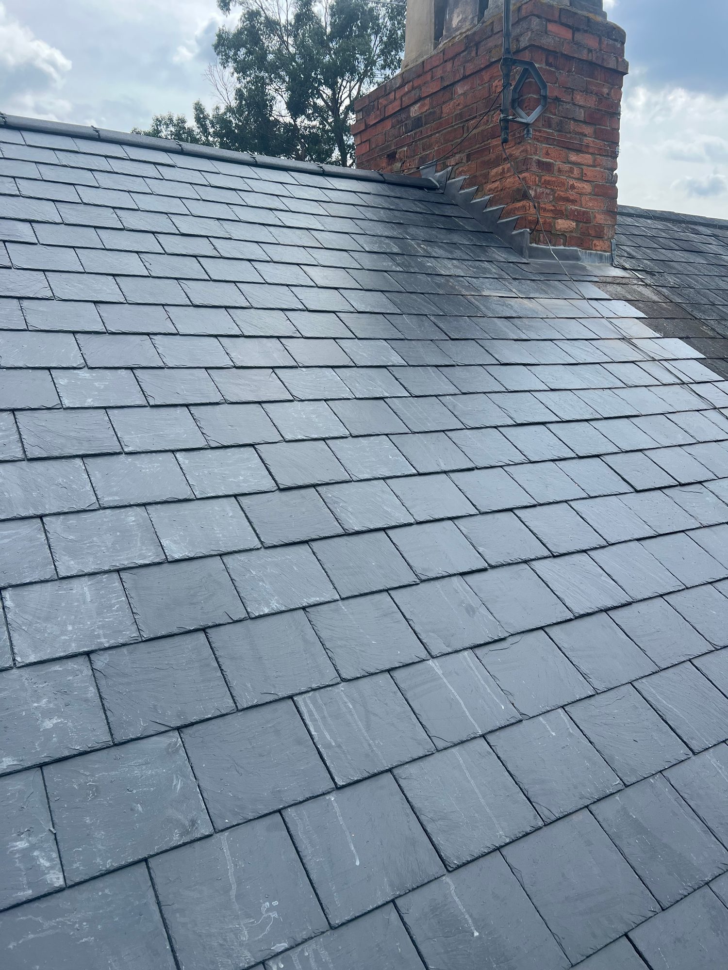 Wide view of the completed slate roof with evenly laid slate tiles and finished detailing around the brick chimney