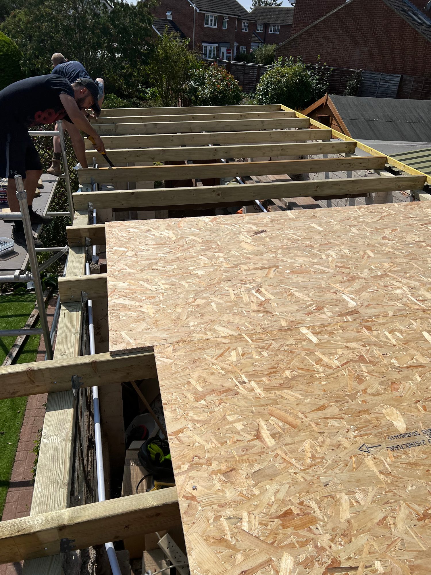 Timber roof joists being installed above the existing structure, with OSB roof decking fitted across part of the roof area