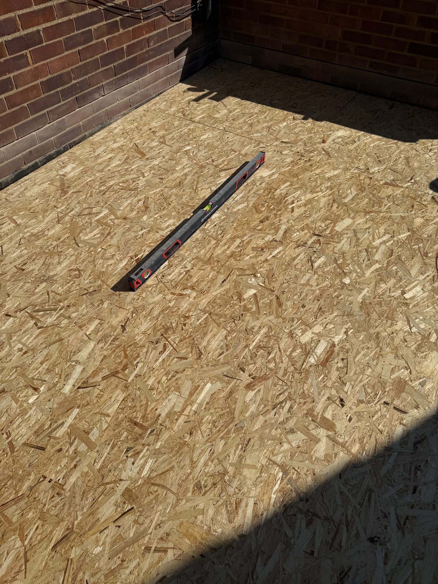 OSB roof decking panels installed across the flat roof area, with a spirit level positioned on the surface and brick parapet walls surrounding the roof space