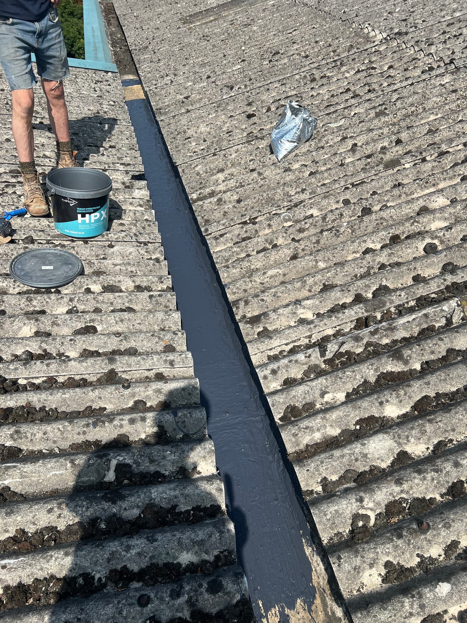 Corrugated roof with a continuous dark waterproofing coating visible along the completed central valley