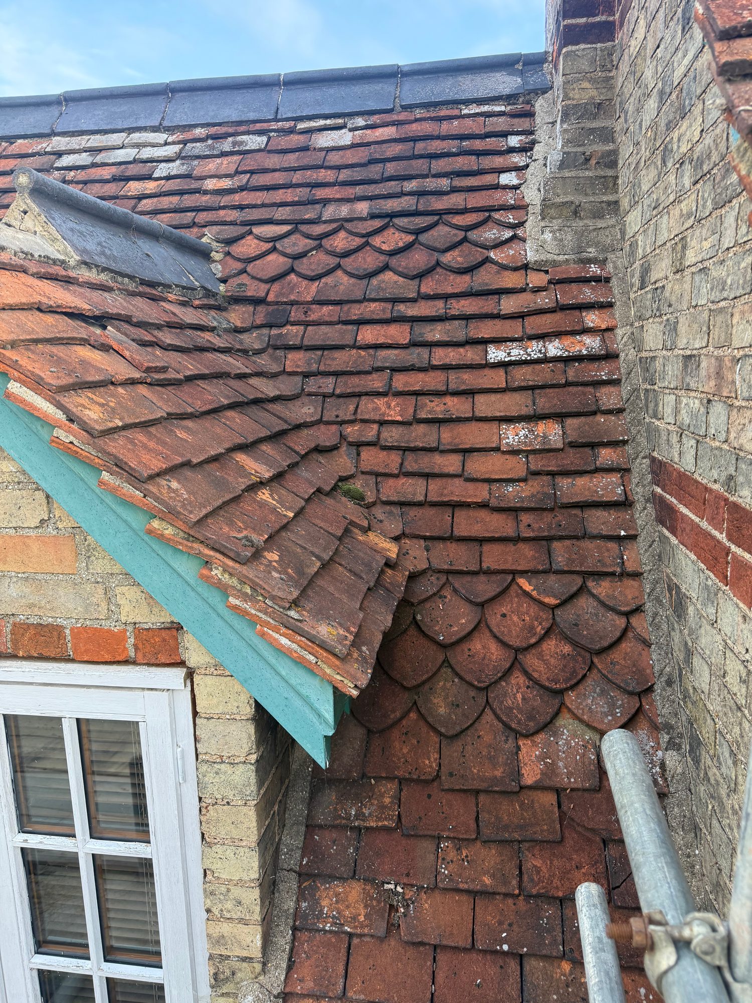 Close-up view of an existing tiled roof showing weathered roof tiles, a roof junction beside the brick wall and a section of guttering and roof edging