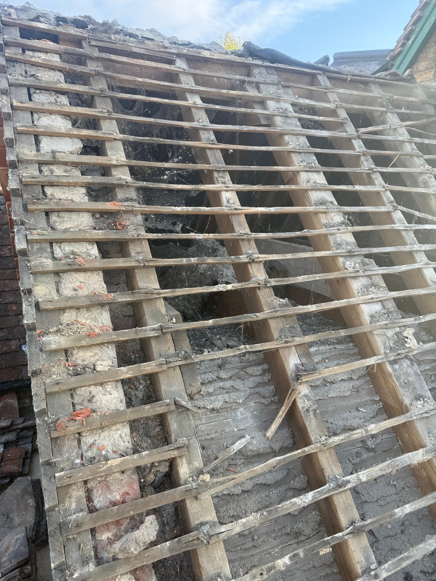 Roof area with tiles removed, showing timber rafters and battens, exposed masonry and the underlying roof structure during construction