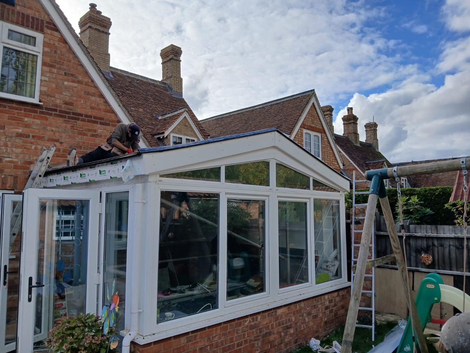 Completed conservatory with a finished white roof edge, glazed panels and doors, with the surrounding brickwork and neighbouring properties visible in the background