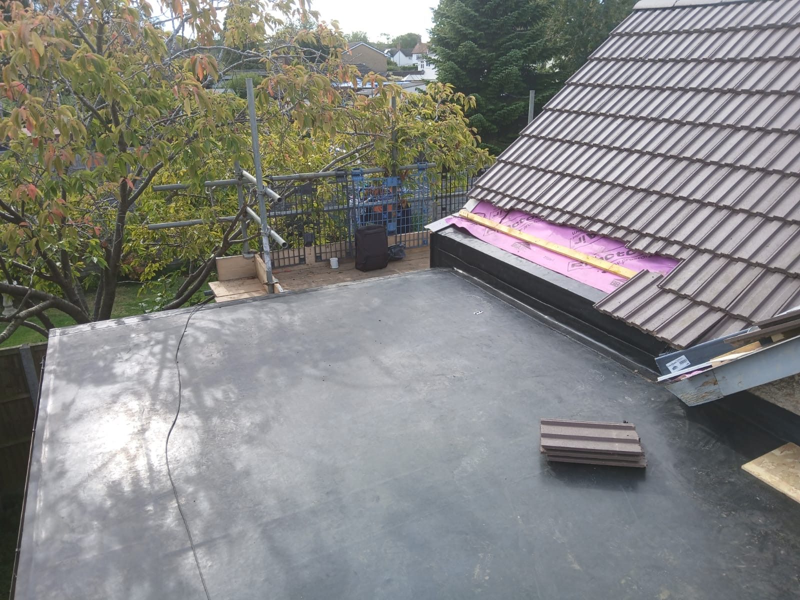 Flat roof area with a newly installed deck, tools and timber visible on the surface, alongside the adjacent pitched tiled roof