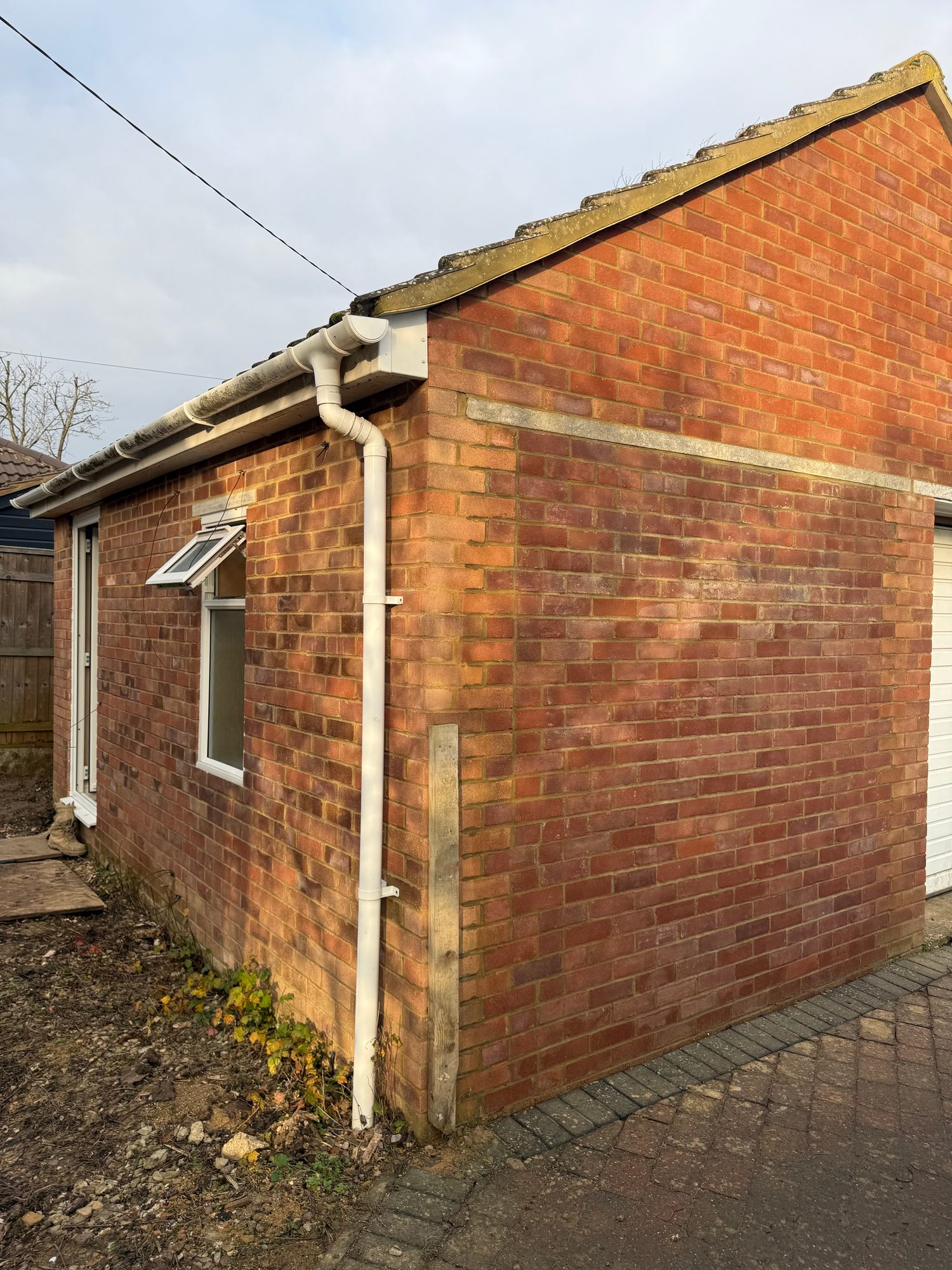 External view of a brick-built extension showing the completed brick walls, roof edge, guttering, downpipe, windows and paved area